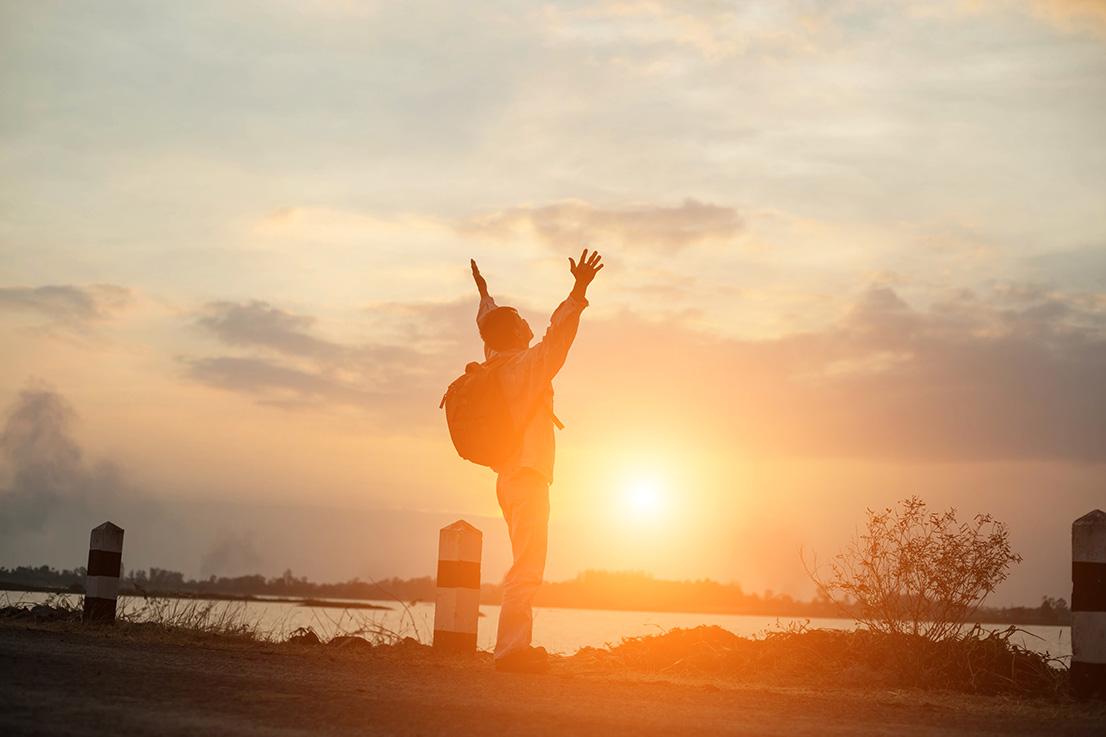 guy standing in front of sunset with his hands up to the sky